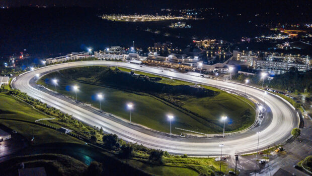 The race track is brightly lit with surrounding buildings visible at night, HD Desktop Wallpaper