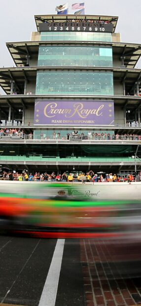A racecar speeds past the Indianapolis Motor Speedway grandstand with spectators watching, HD Mobile Wallpaper