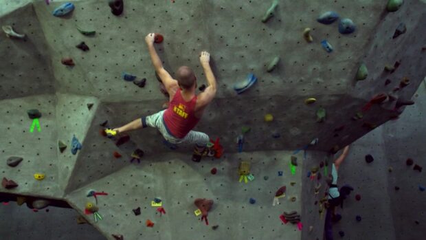 A man in a red shirt climbs challenging routes in a rock climbing gym, HD Desktop Wallpaper
