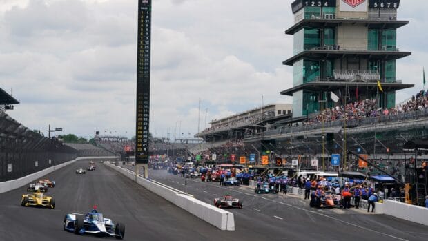 A vibrant IndyCar race with cars speeding by the pit lane at Indianapolis Motor Speedway, HD Desktop Wallpaper