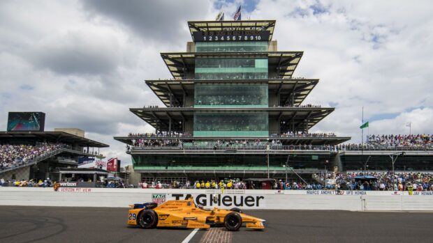 An IndyCar race car speeds past the iconic Indianapolis Motor Speedway grandstand filled with spectators, HD Desktop Wallpaper
