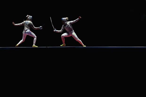 Two fencers compete in a fast paced fencing match on a dark stage, HD Desktop Wallpaper