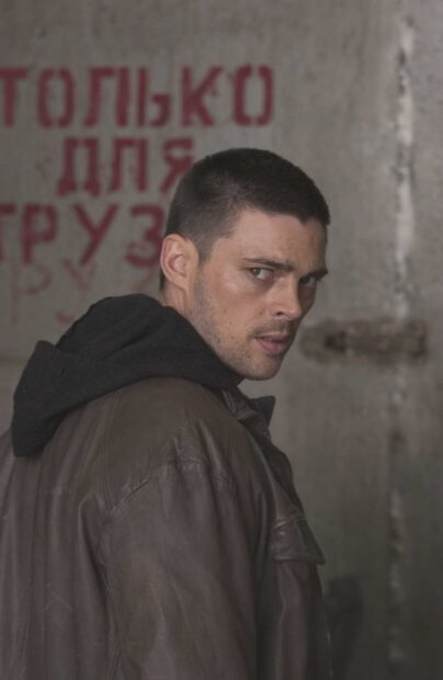 Karl Urban displays a serious expression while wearing a brown jacket and black hoodie, 2K Mobile Wallpaper