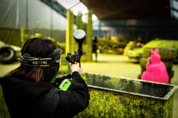 A player wearing a mask aims a paintball gun in an indoor paintball arena, HD Desktop Wallpaper