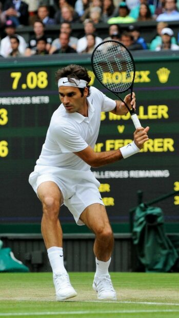 A tennis player is focused during a match on a grass court with a scoreboard in the background, 2K Phone Wallpaper