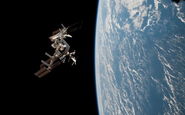 The space station is orbiting above Earth showing its structure and the planet's curved horizon, 2K Desktop Wallpaper