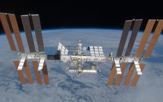 The space station orbits Earth with solar panels and modules visible, 2K Desktop Wallpaper