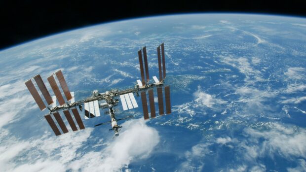 The International Space Station orbits Earth surrounded by blue atmosphere and clouds, HD Desktop Wallpaper