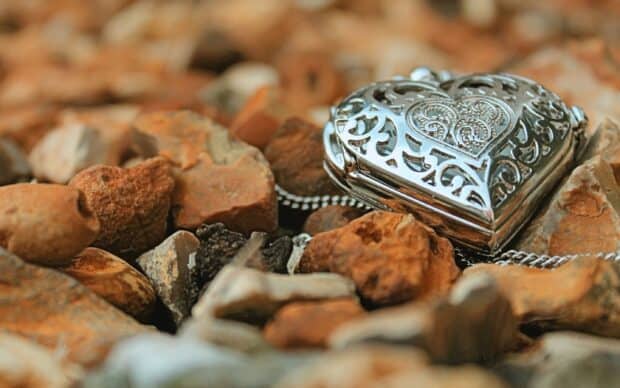 A silver heart shaped jewelry piece lies among rustic stones showing detailed craftsmanship, 2K Desktop Wallpaper