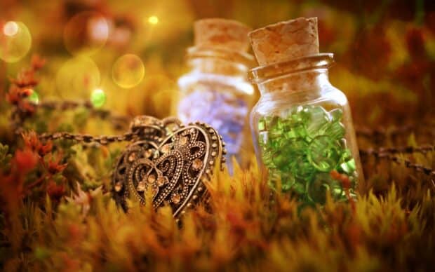 A detailed heart shaped jewelry piece lies among moss near small glass jars, HD Desktop Wallpaper