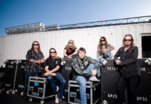 The Iron Maiden band members are seated and standing near equipment cases outdoors, HD Desktop Wallpaper