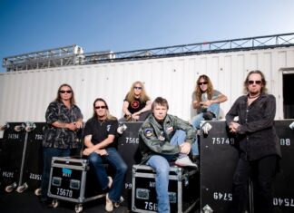 The Iron Maiden band members are seated and standing near equipment cases outdoors, HD Desktop Wallpaper