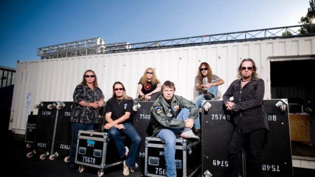 The Iron Maiden band members are seated and standing near equipment cases outdoors, HD Desktop Wallpaper