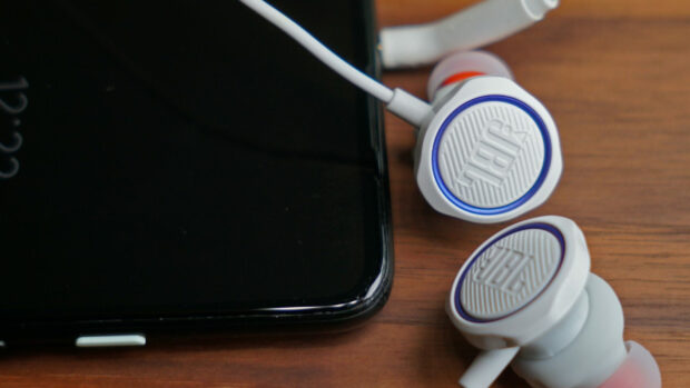 A pair of white JBL earphones connected to a black smartphone lying on a wooden surface, 2K Desktop Wallpaper