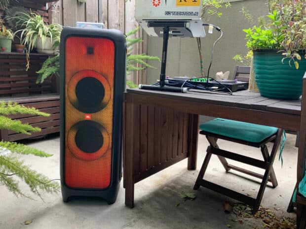 A JBL speaker with glowing orange and red lights stands next to a wooden desk outside, 2K Desktop Wallpaper