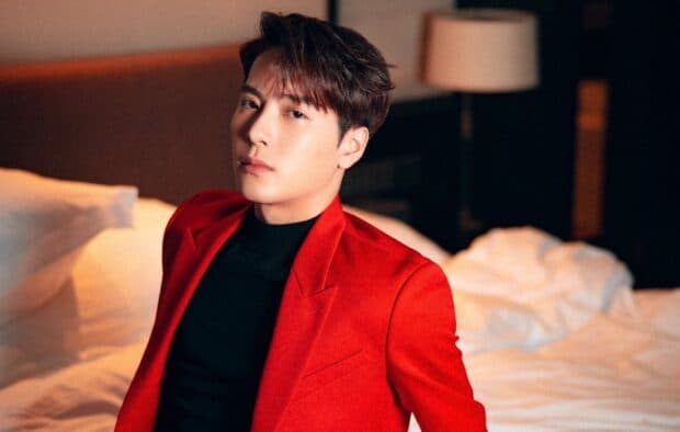 Jackson Wang wears a red jacket while sitting on a bed in a softly lit room, HD Desktop Wallpaper