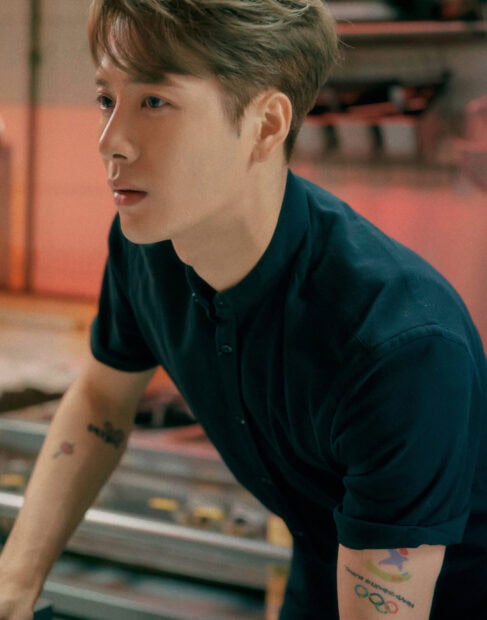 Jackson Wang wallpapers showing him leaning forward with tattoos on his arm, 2K Phone Wallpaper