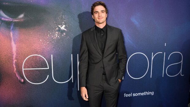 Jacob Elordi stands confidently in a black suit at an event with a colorful backdrop, 2K Desktop Wallpaper