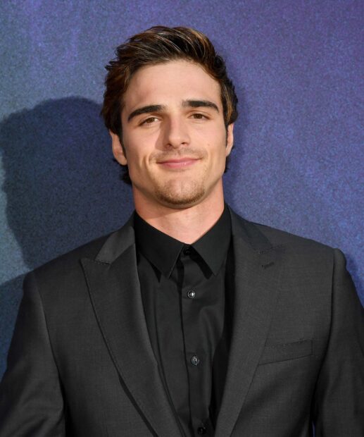 Jacob Elordi smiles confidently wearing a black suit against a blue backdrop, HD Desktop Wallpaper
