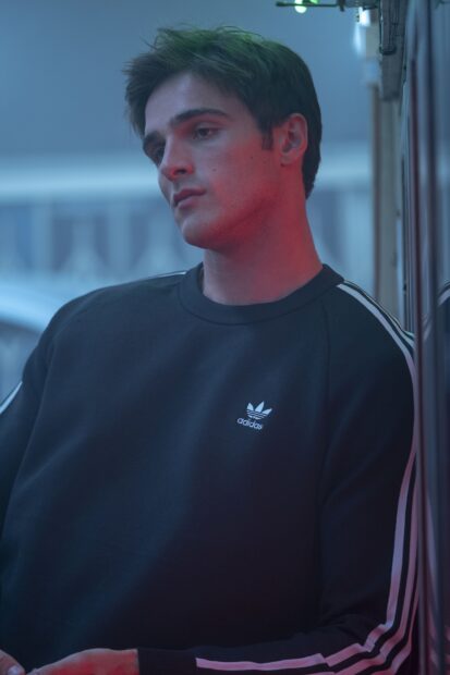 Jacob Elordi looks thoughtful wearing a black Adidas sweater in soft blue and red light, 2K Phone Wallpaper