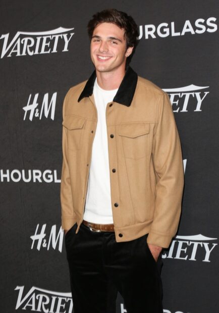 Jacob Elordi smiles wearing a tan jacket and white shirt at an event, HD Desktop Wallpaper