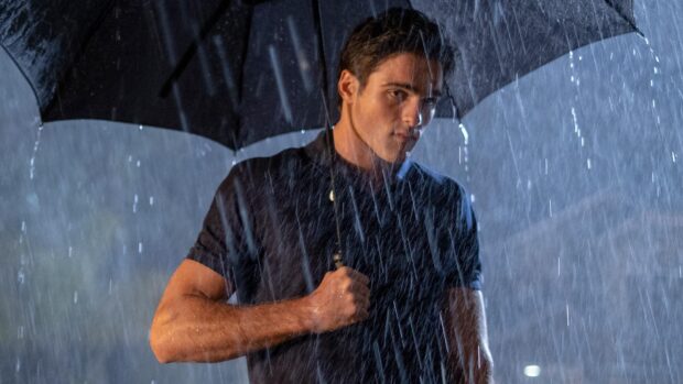 Jacob Elordi stands holding an umbrella while rain falls heavily around him, HD Desktop Wallpaper
