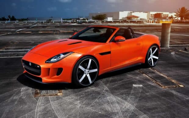 A vibrant orange Jaguar F Type convertible car is parked on a rooftop under a moody sky, HD Desktop Wallpaper