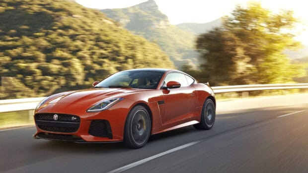 A red Jaguar F Type driving fast on a sunlit road with trees and mountains in the background, 2K Desktop Wallpaper