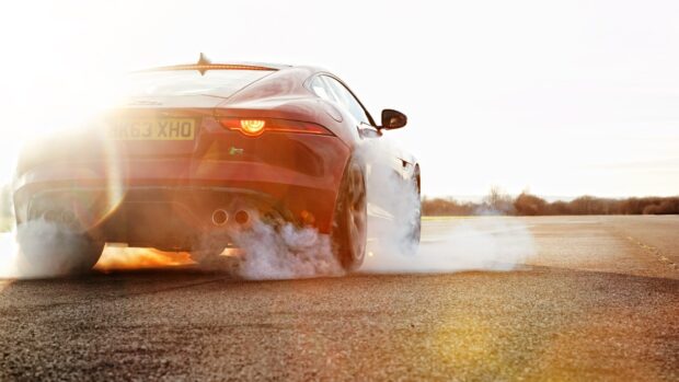 A red Jaguar F Type is performing a burnout on an open road with smoke rising behind, HD Desktop Wallpaper