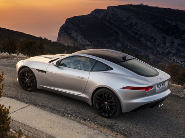 A silver Jaguar F Type is parked on a scenic mountain road at sunset with rugged hills in the background, HD Desktop Wallpaper