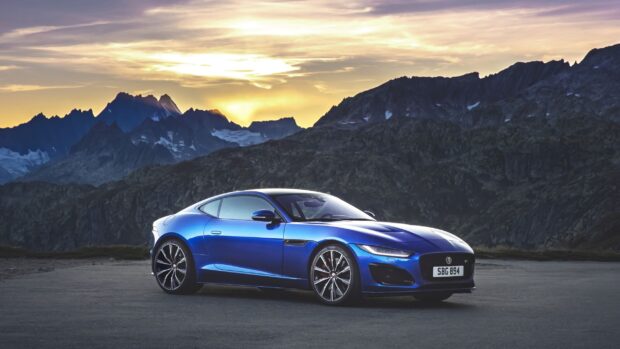 A Jaguar F Type sports car is parked on a mountain road at sunset with dramatic peaks in the background, 2K Desktop Wallpaper