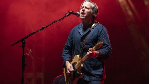 Jason Isbell is playing guitar and singing during a concert with red lighting, HD Desktop Wallpaper