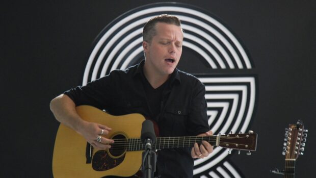 Jason Isbell is playing an acoustic guitar in front of a black and white circular backdrop, HD Desktop Wallpaper