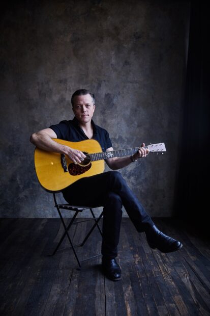 Jason Isbell is sitting on a chair playing an acoustic guitar in a dim room, HD Mobile Wallpaper