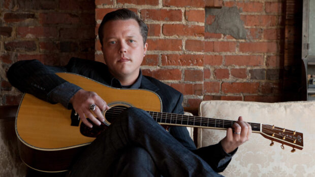 Jason Isbell playing an acoustic guitar while sitting on a couch in front of a brick wall, HD Desktop Wallpaper