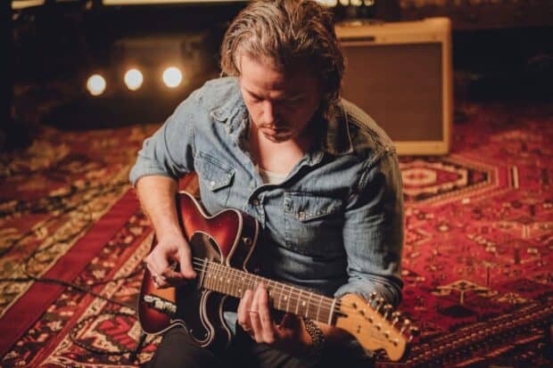 A man named Jason Isbell is focused on playing an electric guitar in a warmly lit music studio, HD Desktop Wallpaper