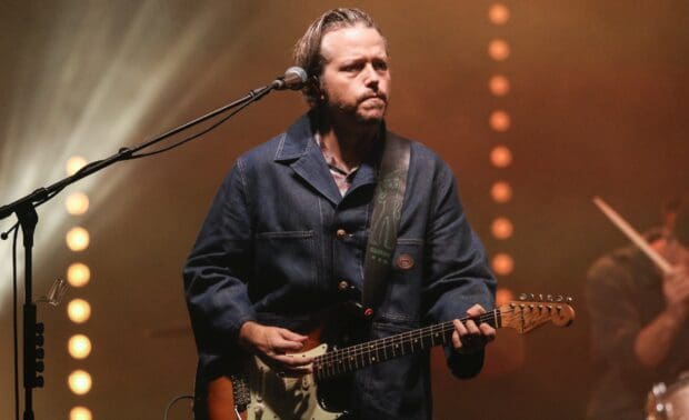 Jason Isbell is focused while playing guitar during a live performance with warm stage lighting, HD Desktop Wallpaper