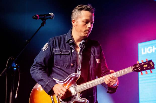 Jason Isbell plays guitar during a live performance with colorful stage lighting, HD Desktop Wallpaper