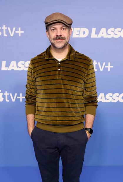 Jason Sudeikis wallpapers shows a man smiling with a brown striped shirt and flat cap, 2K Mobile Wallpaper