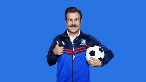 Jason Sudeikis is wearing a blue sports jacket and holding a soccer ball while giving a thumbs up, HD Desktop Wallpaper