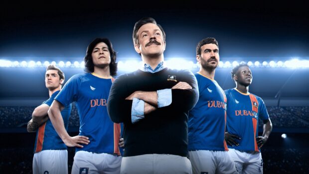 Jason Sudeikis stands confidently with a group of soccer players in a stadium, 4K Desktop Wallpaper