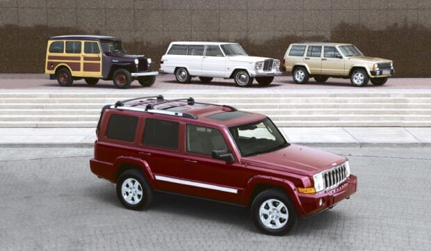 A red Jeep Commander parked on a city street with vintage Jeep models behind it, 2K Desktop Wallpaper