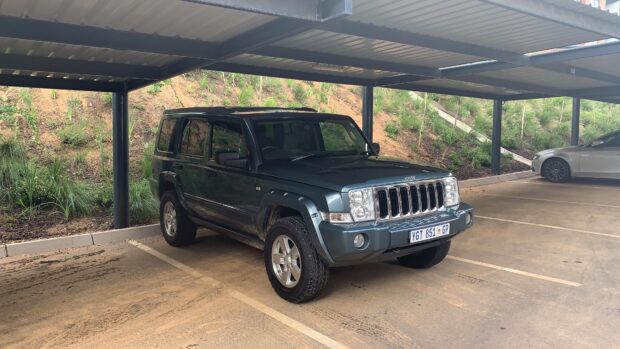 A green Jeep Commander parked under a metal carport with greenery in the background, 4K Desktop Wallpaper