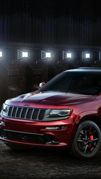 A red Jeep Grand Cherokee is parked indoors with bright lights behind it, 2K Mobile Wallpaper