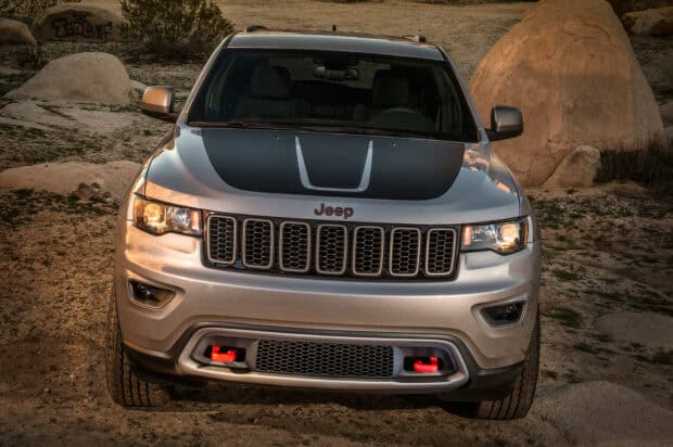 A silver Jeep Grand Cherokee with headlights on is parked on a rocky terrain, HD Desktop Wallpaper