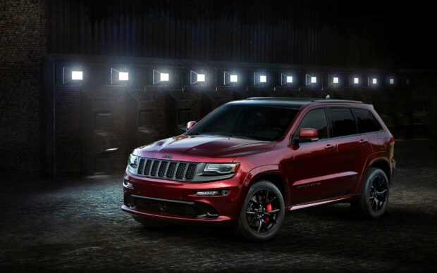 A red Jeep Grand Cherokee is parked in a dimly lit environment with striking lighting effects, 2K Desktop Wallpaper