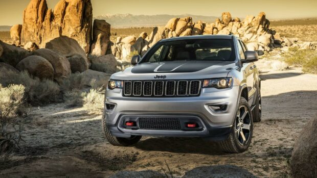 A Jeep Grand Cherokee drives through a rocky desert with large boulders in the background, 2K Desktop Wallpaper