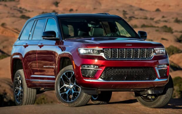 A red Jeep Grand Cherokee is parked on rocky desert ground under clear skies, HD Desktop Wallpaper