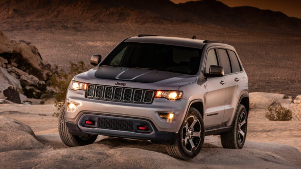 A Jeep Grand Cherokee drives on rocky terrain with desert mountains in the background, 4K Desktop Wallpaper