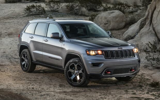 A gray Jeep Grand Cherokee is parked on rocky desert ground with headlights on, HD Desktop Wallpaper